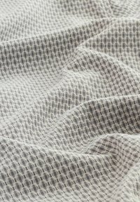 Lekki, teksturowany materiał z subtelnym geometrycznym wzorem w odcieniach szarości na przezroczystym białym tle, ukazujący delikatny, płynny kształt.