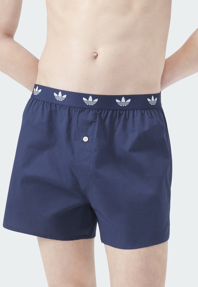 Marineblaue Shorts mit einem elastischen Bund, verziert mit weißen Adidas-Trefoil-Logoakzenten, einem Frontknopf und einer glatten Textur.