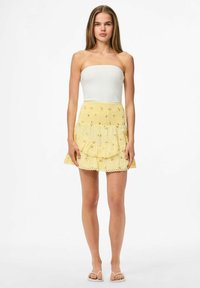 Minifalda amarilla con flores, con volantes y bordes de encaje, combinada con un top ajustado sin mangas blanco. Textura suave y tela blanda.