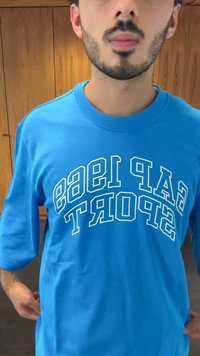 T-shirt de algodão azul com manga curta. Apresenta texto branco que diz "CAP 1953 SPORT" num design curvado na parte da frente. Design simples e casual.