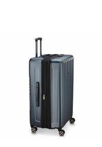 Valise rigide gris foncé avec un design nervuré, deux roues, une poignée rétractable et un compartiment zippé noir. Des accents incluent une tirette de fermeture éclair jaune.