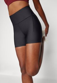 Pantaloni sportivi neri con vita alta, materiale elastico, texture liscia e ritagli laterali vicino all'orlo inferiore per la ventilazione.
