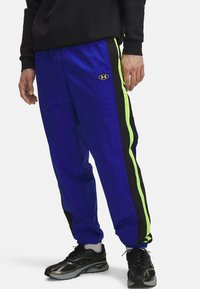 Blauwe nylon trainingsbroek met zwarte en neon groene zijstrepen; voorzien van een geborduurd logo nabij de taille; elastische tailleband en boorden.