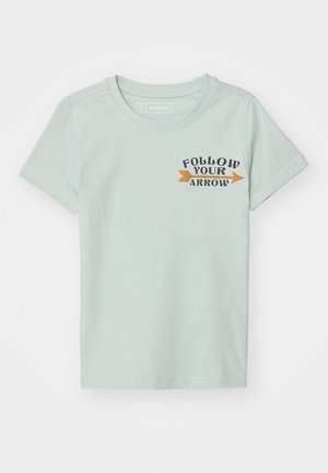 Camiseta de manga corta de color verde claro con cuello redondo y texto "SIGUE TU FLECHA" junto a una flecha naranja que apunta a la derecha en el lado izquierdo del pecho.