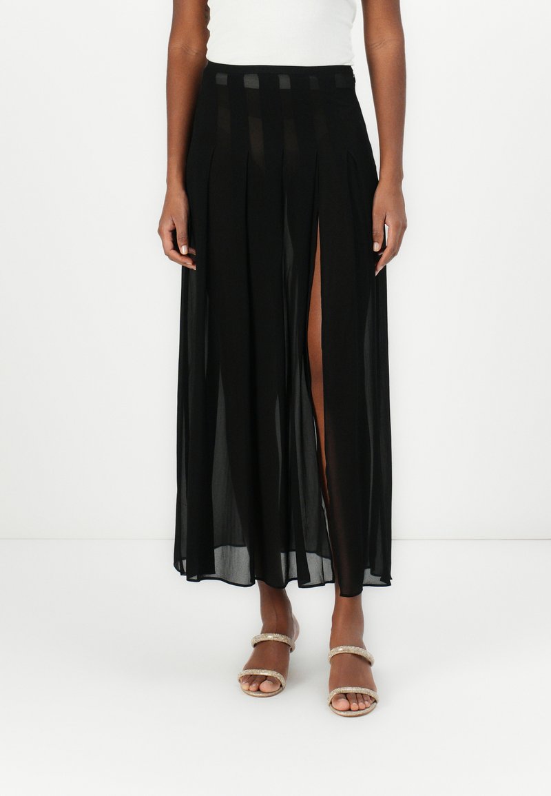 Gonna maxi nera a plissettature con pannelli trasparenti, caratterizzata da uno spacco laterale alto fino alla coscia e una vita con accenti a righe orizzontali. Texture liscia.