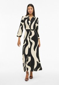 Dolga črna in smetana obleka z gumbnim zapenjanjem spredaj, ovratnikom, rokavi do treh četrtin in valovnim vzorcem, izdelana iz lahkega blaga.