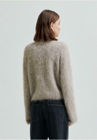 Ljust grått, fluffigt rundhalsat tröja med lös passform och långa ärmar, kombinerat med mörka denimjeans.