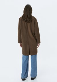 Brącoat z wełny w oversize'owym fasonie, prostego kroju, z długimi rękawami i szwem z tyłu, zestawiony z szerokimi niebieskimi dżinsami. Gładka faktura, casualowy styl.