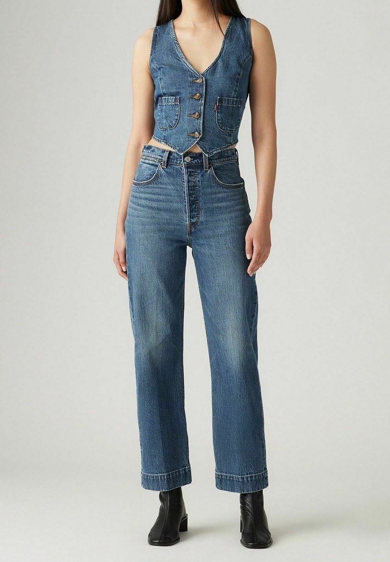 Combinaison en denim avec un corsage ajusté, un col en V, des boutons et deux poches avant ; jambes larges, taille haute avec un lavage clair et des détails d'ourlet effiloché.