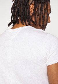 Vit bomullströja med rund halsringning och korta ärmar. Tyget verkar ha en lätt strukturerad yta med en avslappnad passform.