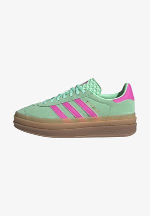 Zielony zamszowy sneaker Adidas z różowymi paskami, gumową warstwową podeszwą i złotym napisem "GAZELLE" z boku.