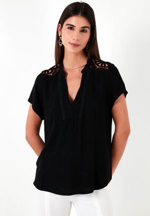 Black short-sleeved blouse with a V-neck, featuring lace accents on shoulders and detailed trim along the neckline and front pleat.