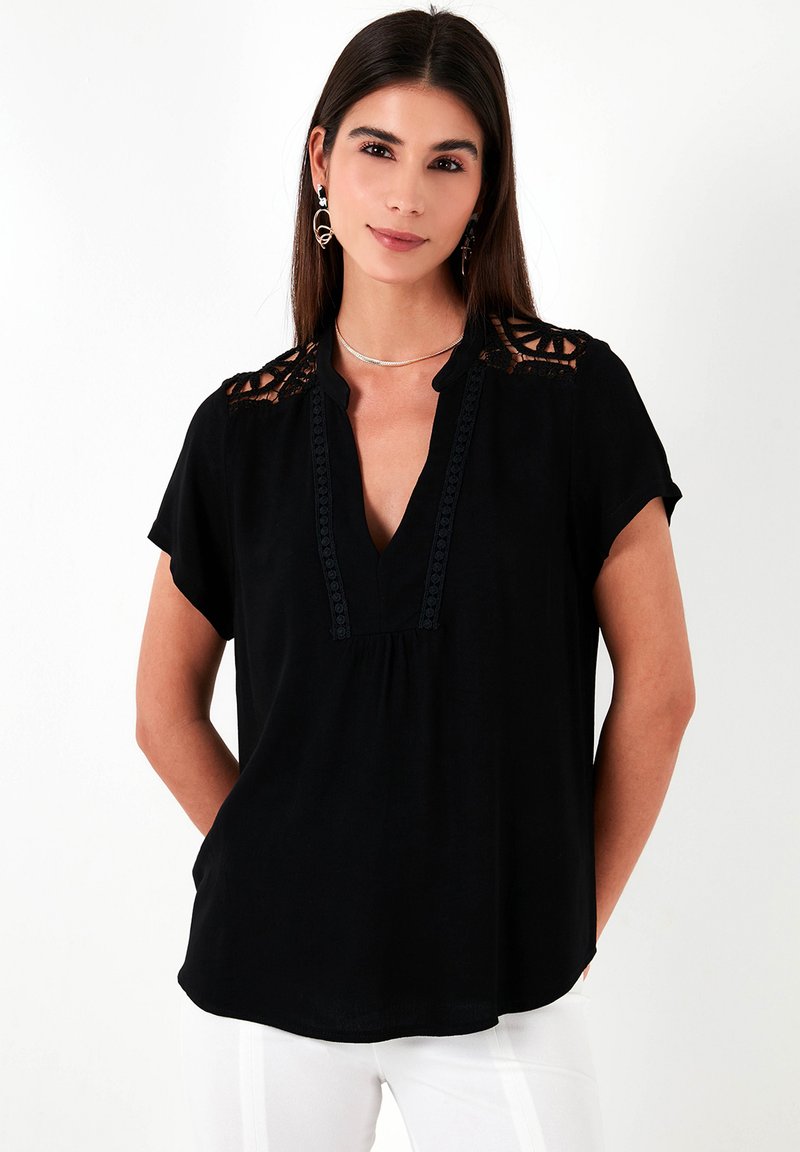 Blusa nera a maniche corte con scollo a V, caratterizzata da inserti in pizzo sulle spalle e dettagli lungo il collo e la plissettatura frontale.