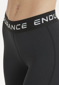 Schwarze Leggings mit glatter Textur und tailliertem Design. Der Bund zeigt ein weißes "ENDURANCE"-Logo.
