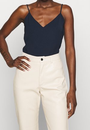 Marineblå ærmeløs top med V-hals og spaghettistropper, kombineret med cremefarvede, højttaljede bukser med knapper foran og glat tekstur.