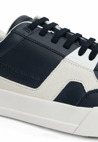 Granatowe skórzane sneakersy z zamszowymi akcentami, białą gumową podeszwą i czarnymi sznurówkami. Posiadają teksturowane wzory oraz logo marki z boku.