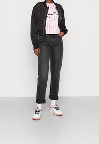 Svart bomberjacka över en rosa randig t-shirt, i kombination med rullade svarta jeans och vita sneakers med rosa detaljer och svarta snören.