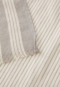 Gråstripet tekstil med en myk, vevd tekstur. Har fransede kanter og en kremfarget bakgrunn med tynne, lysegrå striper.