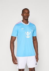 Camisola de futebol azul-claro de manga curta com detalhes cor-de-rosa e riscas verticais, apresentando um logótipo branco de âncora e um decote redondo.