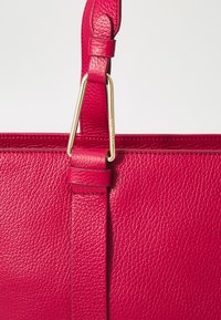 Bolsa de mão em couro vermelho com acabamento texturizado, apresentando um detalhe de fecho em metal dourado e alças para uma fixação segura.
