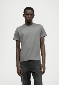 T-shirt cinza de algodão com mangas curtas, apresentando um decote rounded e um logótipo branco "REPLAY" impresso no peito. Combinado com jeans escuros.