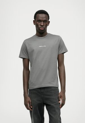 T-shirt cinza de algodão com mangas curtas, apresentando um decote rounded e um logótipo branco "REPLAY" impresso no peito. Combinado com jeans escuros.