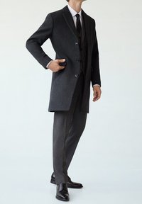 Koolgrijze wollen jas met notch-lapels, een enkelrijks ontwerp en twee knopen. Gecombineerd met een gestreept grijs kostuum en zwarte leren schoenen.