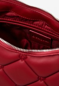 Red quilted leather bag interior with a smooth satin lining, featuring a zip closure and a small embossed brand label.