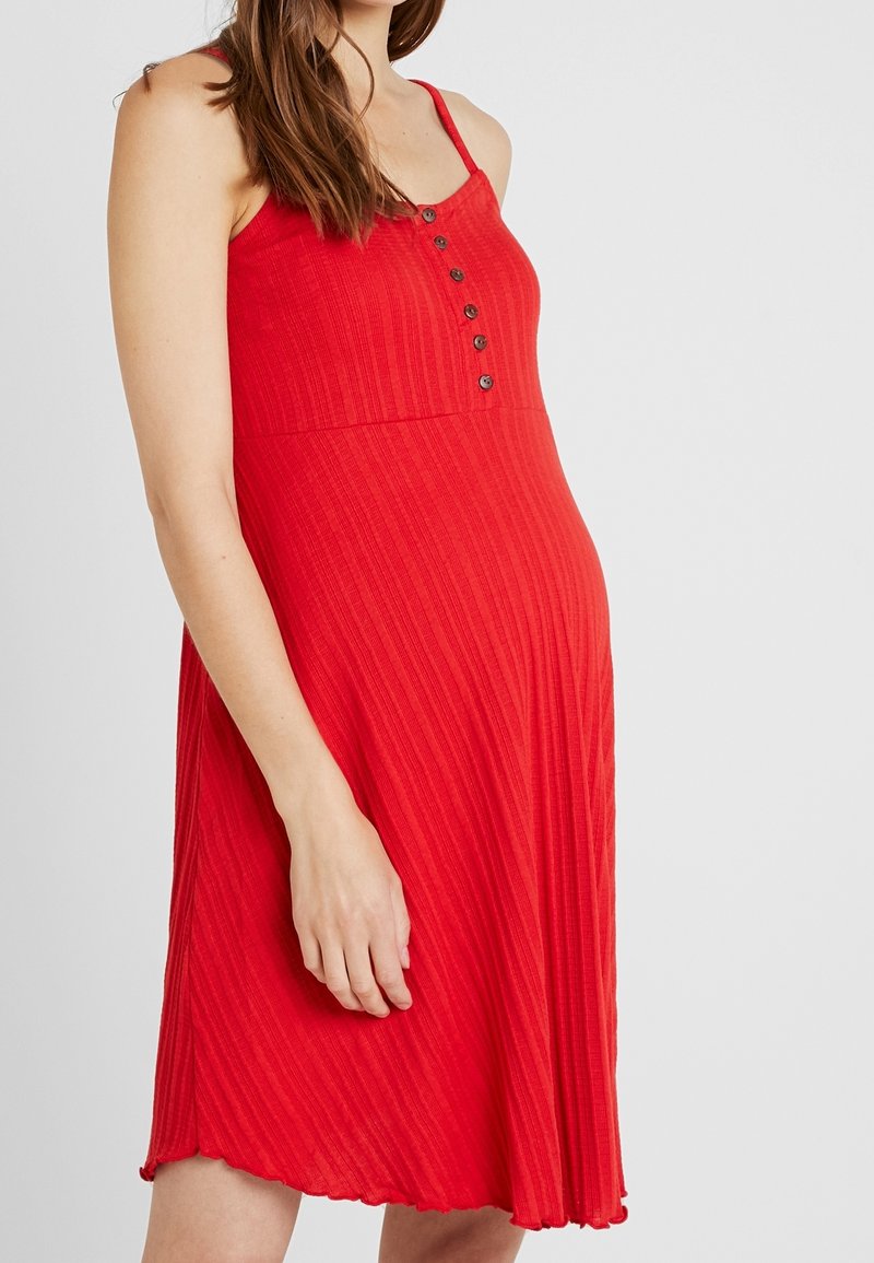 Robe rouge à côtes avec des bretelles spaghetti réglables et un devant boutonné. Tissu fluide avec un ourlet à volants. Adaptée à diverses occasions.