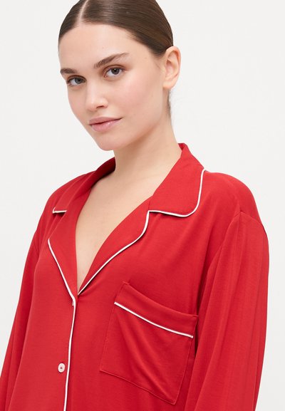 Red pajama top with a V-neck and white piping. Features long sleeves and a breast pocket. Soft fabric texture, relaxed fit.