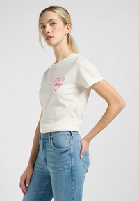 Hvid bomulds T-shirt med et rosa hjertegrafik med teksten "Lee" og "1890". Kortærmet og med en klassisk rund hals.
