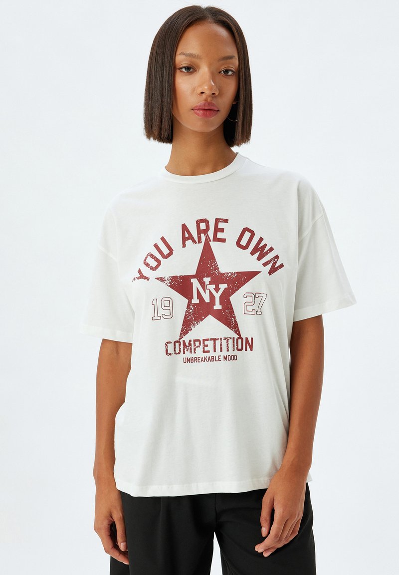 Camiseta blanca de algodón con estampado gráfico rojo que presenta una estrella, el texto "TÚ ERES PROPIO" y "COMPETENCIA". Cuello redondo, mangas cortas, corte relajado.