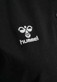 Zwart katoenen poloshirt met een wit bijenlogo en de tekst "hummel" op het linkerborstgebied, met een textuur aan het oppervlak.