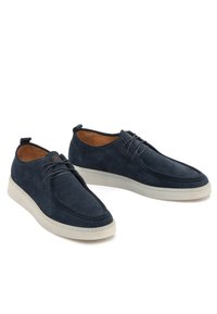 Scarpe in suede blu navy con una texture liscia, suola in gomma bianca e dettagli delle stringhe tonali. Forma arrotondata e cuciture lungo i bordi.