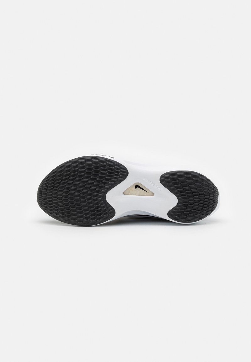 Semelle d'une chaussure de sport blanche avec des grips en caoutchouc noir texturé et un petit logo Nike visible à travers une partie centrale transparente.