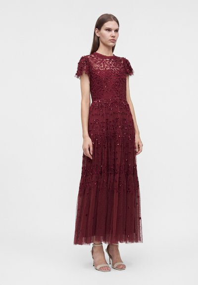 Femme portant une robe bordeaux longue jusqu'au sol avec des détails en dentelle florale et des manches courtes, associée à des escarpins ouverts beige.