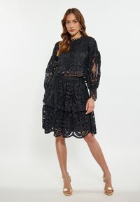 Completo in pizzo nero in due pezzi con top corto a maniche lunghe a palloncino e una gonna a strati, che mostra intricate fantasie floreali.