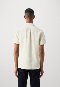 Beige kortermet skjorte laget av teksturert stoff, med en myk krage og en avslappet passform, brukt med mørk denimjeans.