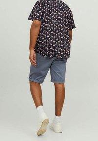 Camisa de manga corta azul marino con un patrón de flamencos rosas, combinada con pantalones cortos grises y zapatillas blancas, con dobladillos enrollados y calcetas hasta la pantorrilla.