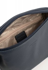 Interno di una borsa in pelle blu scuro con fodera beige, dotata di una tasca con zip e un piccolo etichetta in pelle nera. Texture liscia, forma strutturata.