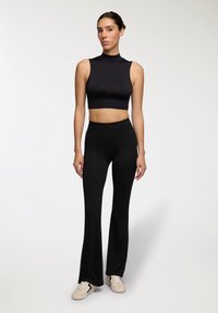 Czarny bezrękawnik z wysokim dekoltem, w połączeniu z czarnymi spodniami z wysokim stanem i rozszerzanymi nogawkami. Gładki, elastyczny materiał o eleganckim fasonie.