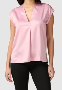Blouse en satin rose avec un décolleté en V et des manches courtes roulées, dotée d'un pli à l'avant et d'extensions sur les côtés à l'ourlet.