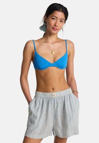 Haut de bikini bleu texturé avec fines bretelles, associé à un short léger à rayures, à la coupe décontractée et à la taille élastique.