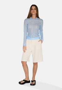 Ljust blå långärmad topp med en texturerad yta, kombinerad med beige knälånga shorts och svarta flip-flop sandaler.
