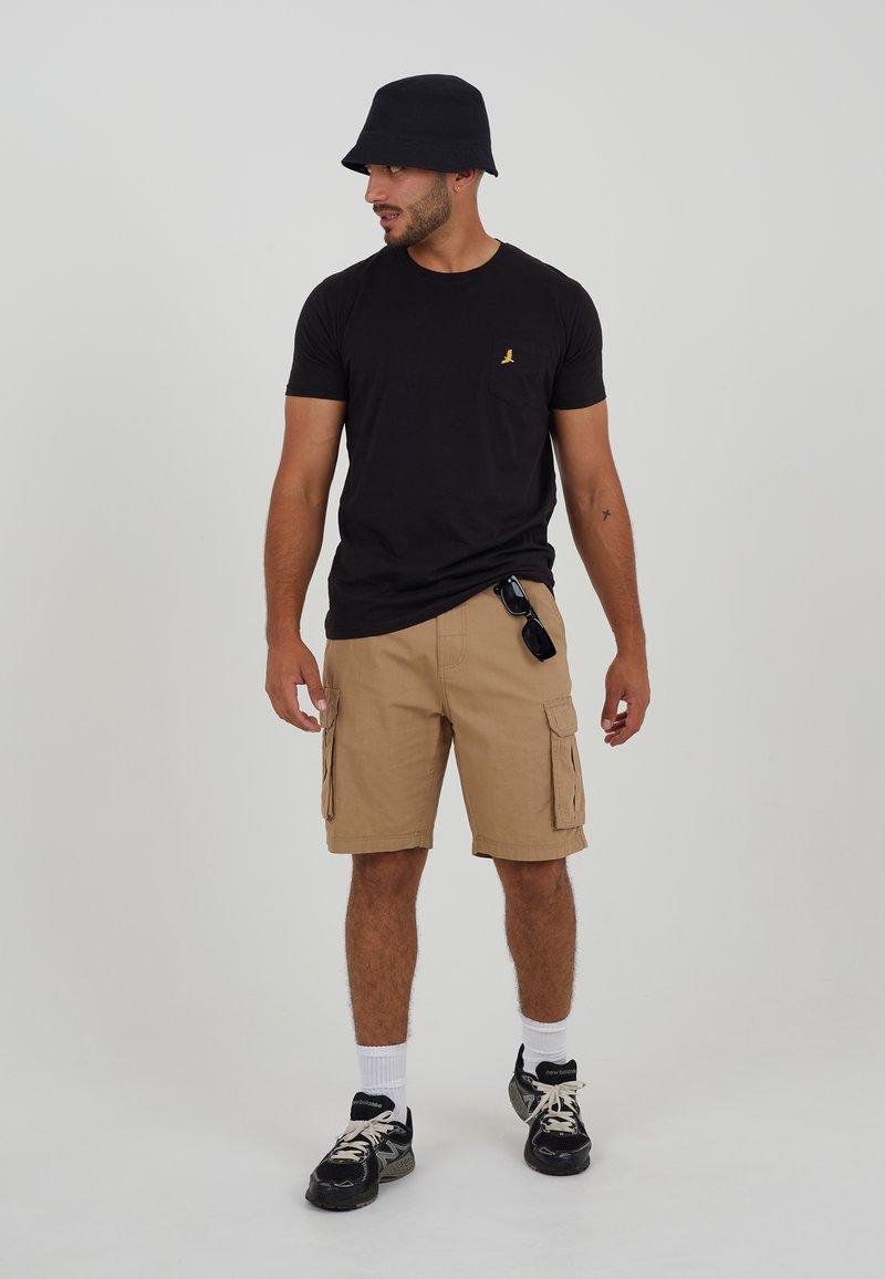 Black t-shirt with a chest pocket, tan cargo shorts with side pockets, black bucket hat, and black sneakers with white accents.