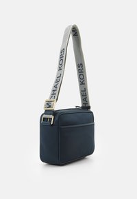 Marineblå crossbody taske lavet af glat materiale; har en stribet skulderrem med logo, guldfarvet metal, og lynlås lukning.