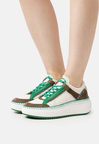 Baskets avec un mélange de mesh blanc, de daim marron et d'accents verts. Semelle épaisse blanche avec rainures texturées et design de lacets unique.
