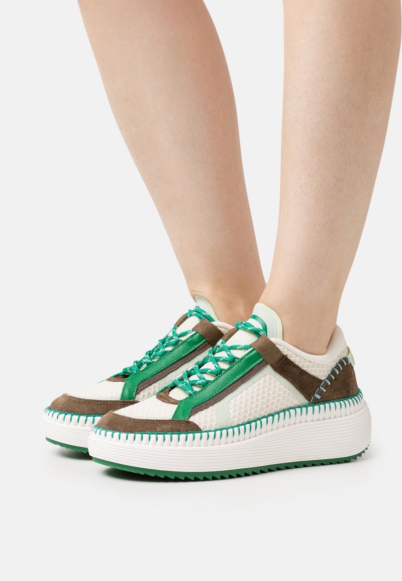 Baskets avec un mélange de mesh blanc, de daim marron et d'accents verts. Semelle épaisse blanche avec rainures texturées et design de lacets unique.
