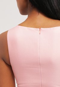 Vaaleanpunainen hihaton mekko, jossa on pyöreä pääntie ja keskellä selässä oleva vetoketju, jossa on koristeellinen vetotappi. Sileä, hieman kiiltävä kangas.