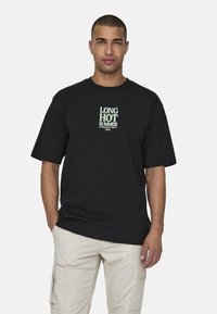 Czarna koszulka bawełniana z białym i zielonym napisem "DŁUGIE GORĄCE LATO" w prostym kroju. Okrągły dekolt, krótki rękaw.